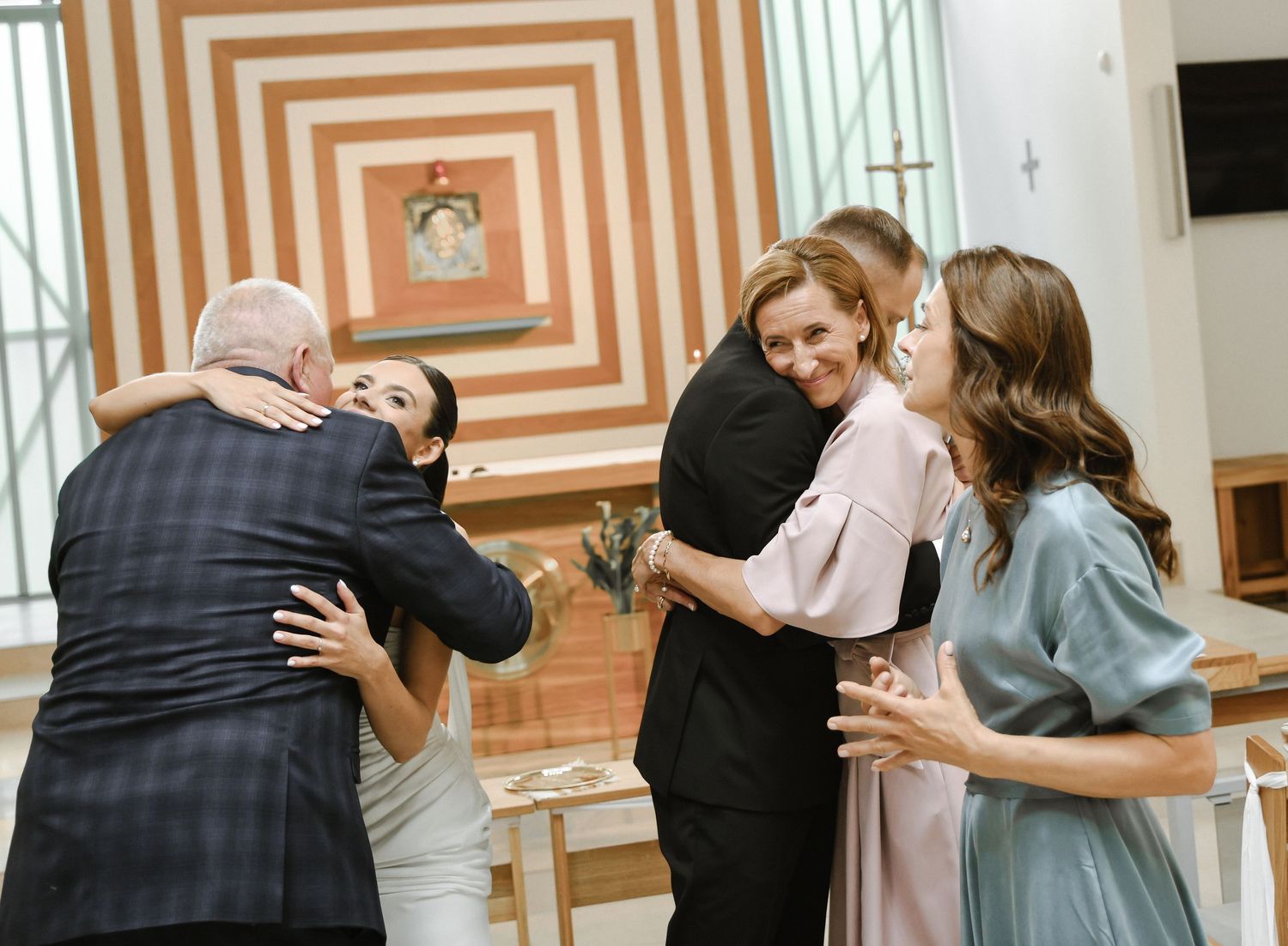 Wedding party members hug and celebrate in a church with orange striped walls.