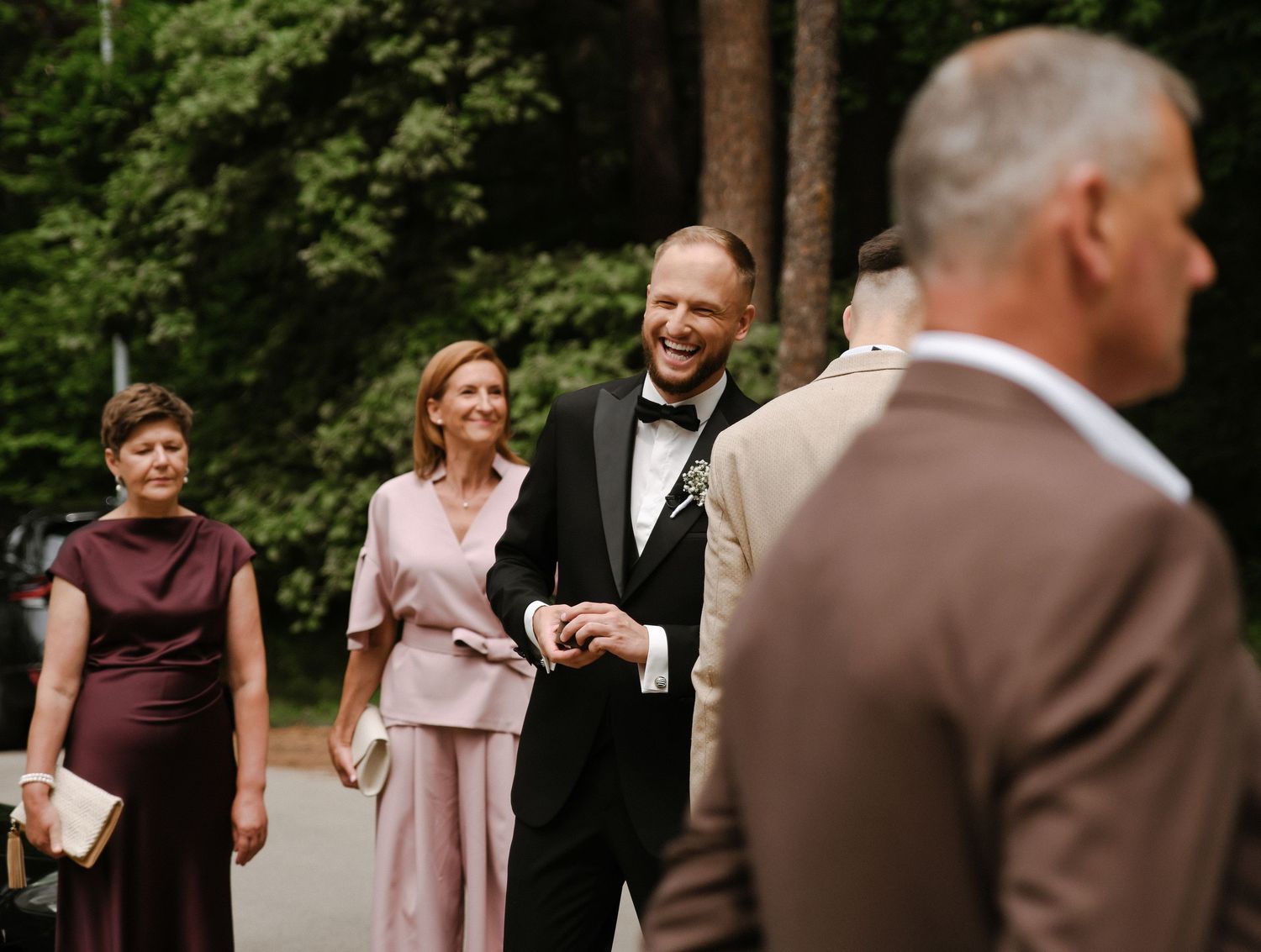 Wedding party members in burgundy and blush pink dresses celebrate outdoors in a joyful moment.