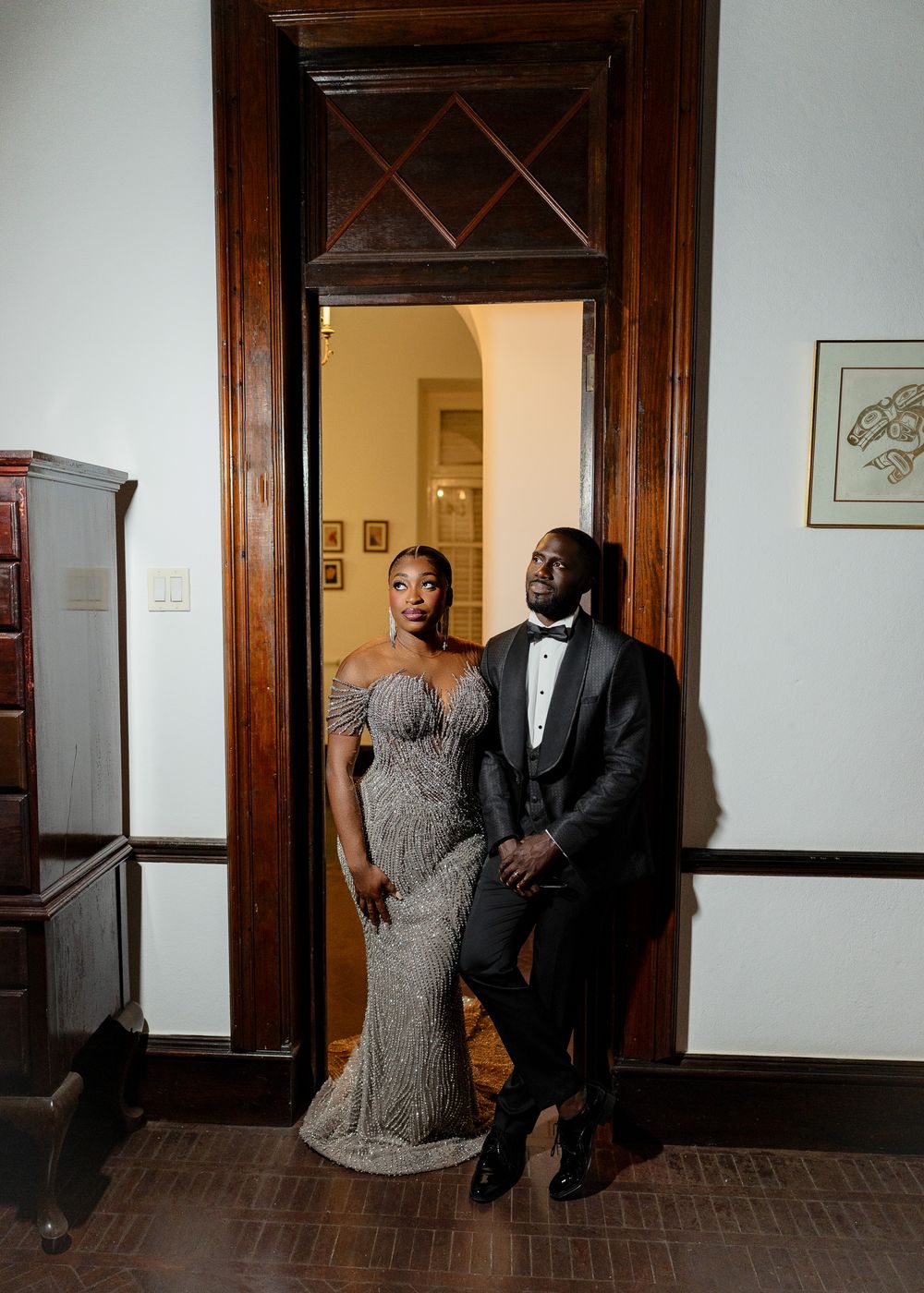 A couple shares a sweet candid moment together in a hallway with dark wood trim and white walls.