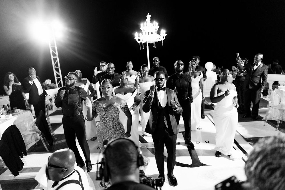 Black and white panoramic collage of people dancing at a wedding reception under elegant chandeliers.