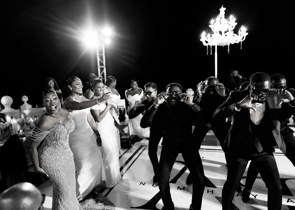 Wedding guests dance together on an outdoor dance floor at night under a glowing chandelier and bright spotlights.
