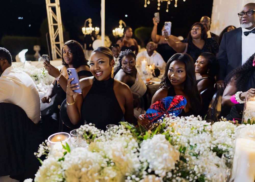 Wedding guests seated at elegant tables with white floral centerpieces enjoy a reception celebration.