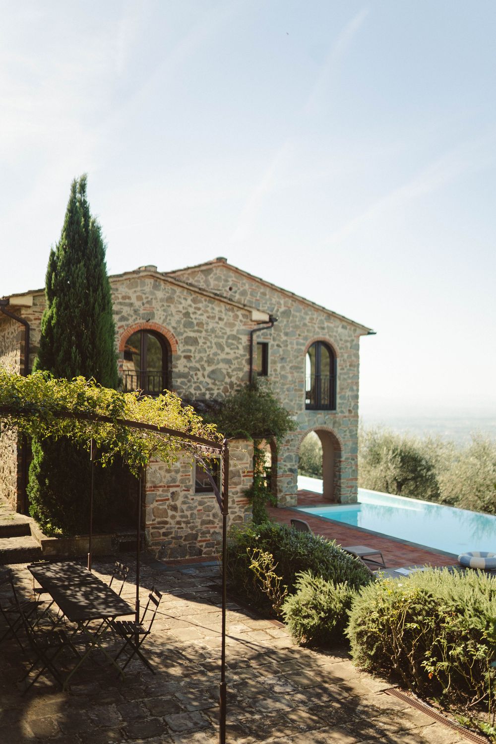 Rustic stone villa with infinity pool overlooking Tuscan countryside and cypress trees.