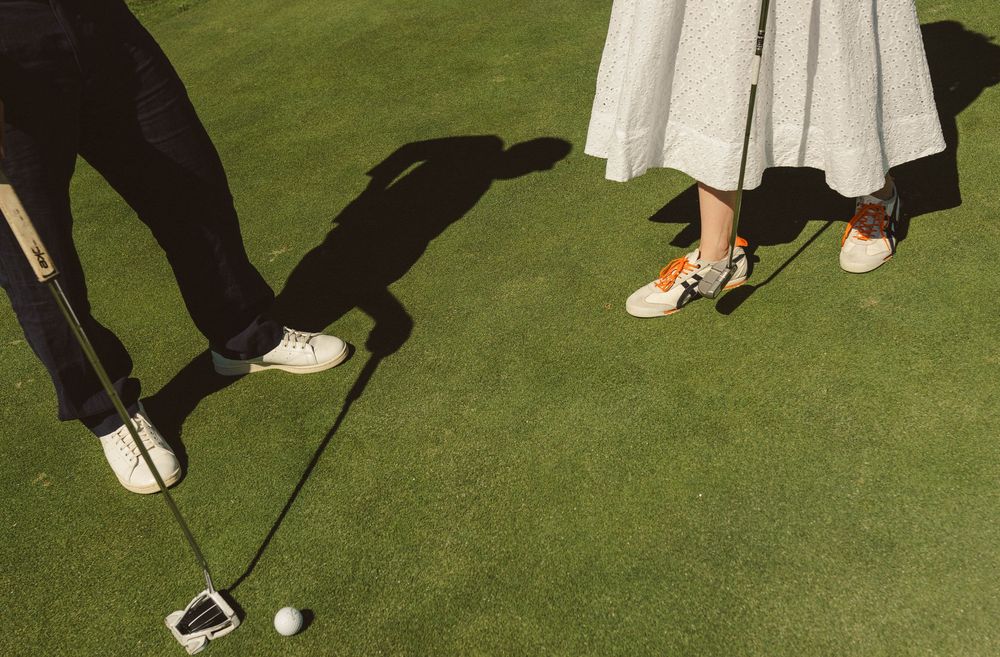 Two pairs of feet on a golf green with a putter and golf ball.