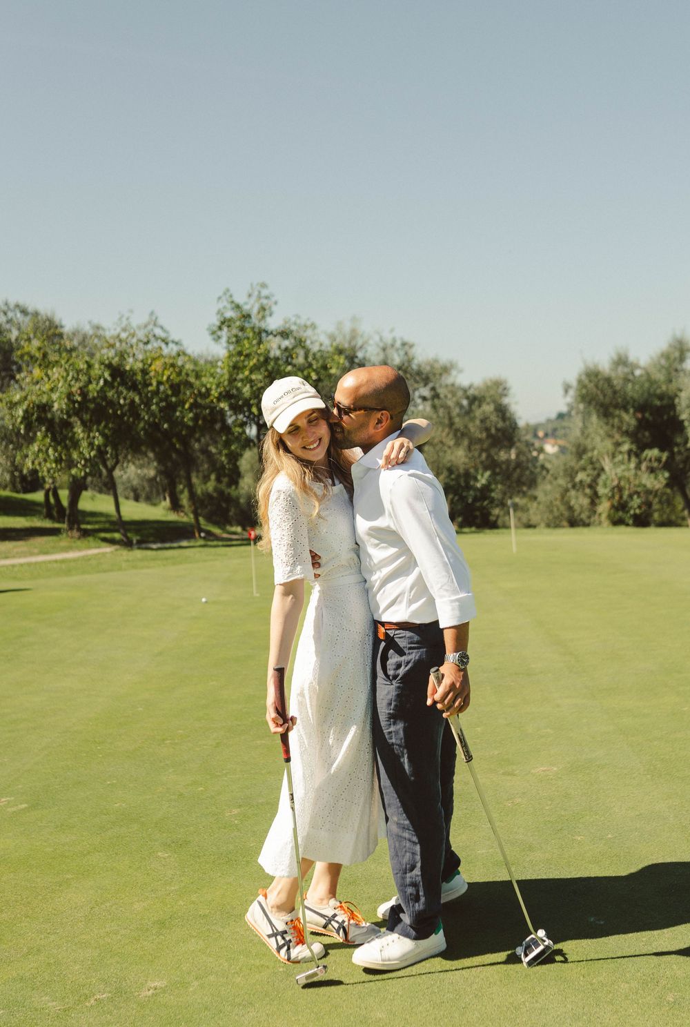 A romantic moment between a couple on a golf course surrounded by olive trees.