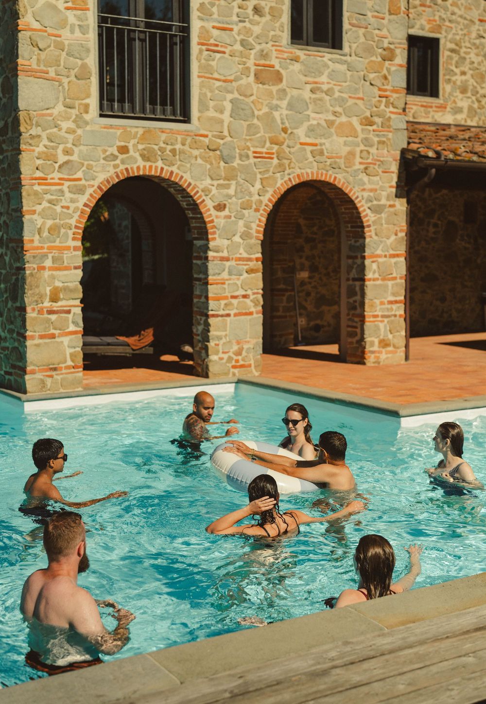 People enjoying a refreshing swim in a pool surrounded by rustic stone architecture.