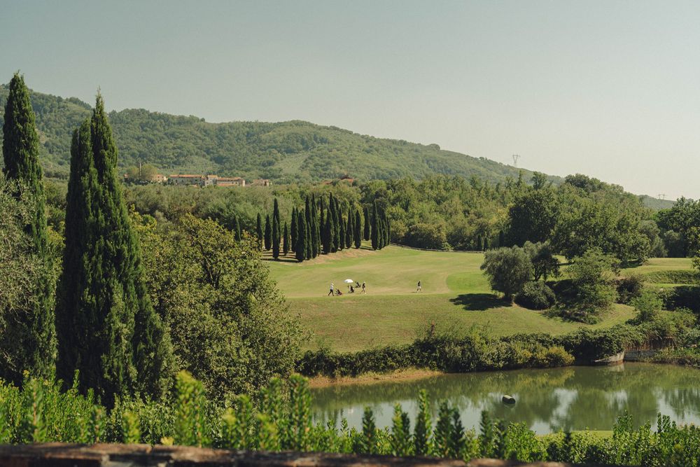 Panoramic view of rolling Tuscan hills with cypress trees and a serene lake.