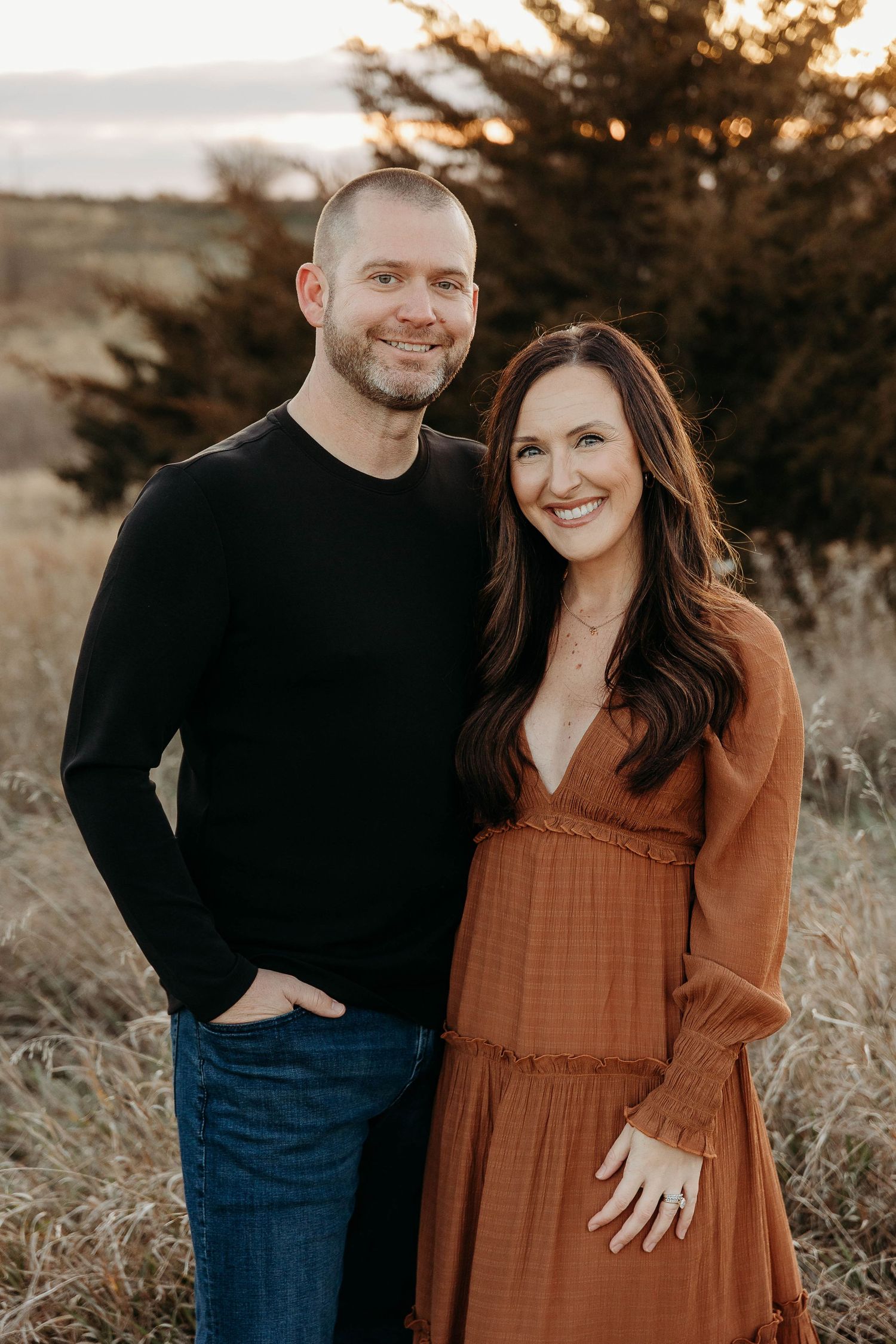 A couple poses together outdoors in a romantic autumn photoshoot with warm lighting and tall grass.