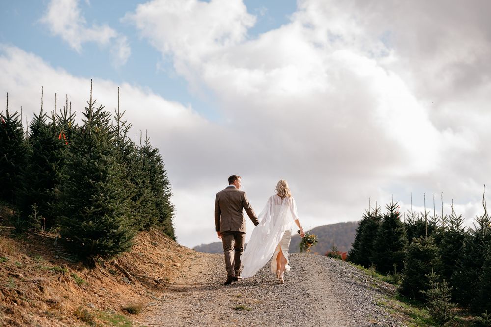 A couple walks along a mountain trail with dramatic cloudy skies overhead.