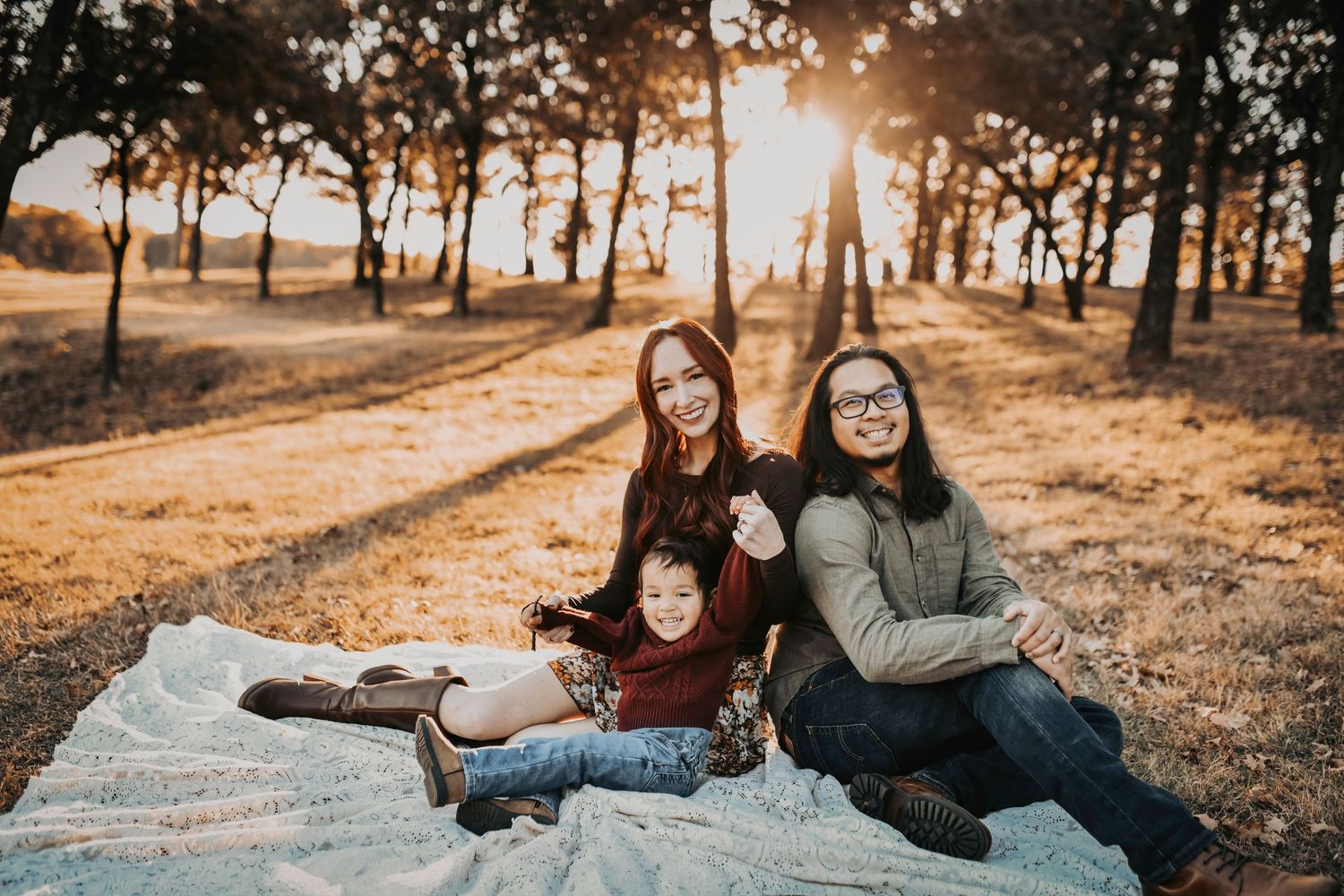 Parents cuddling their toddler son in cozy fall layers during a sunset family session.