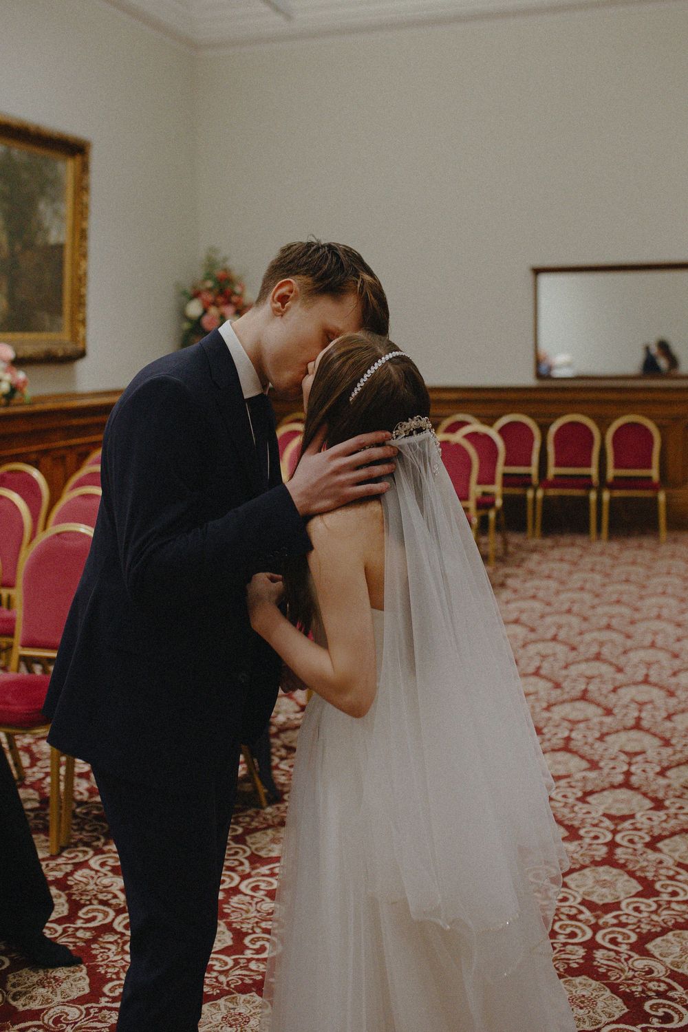 A sequence of four wedding photos showing a romantic kiss between newlyweds in an elegant room with red carpeting.
