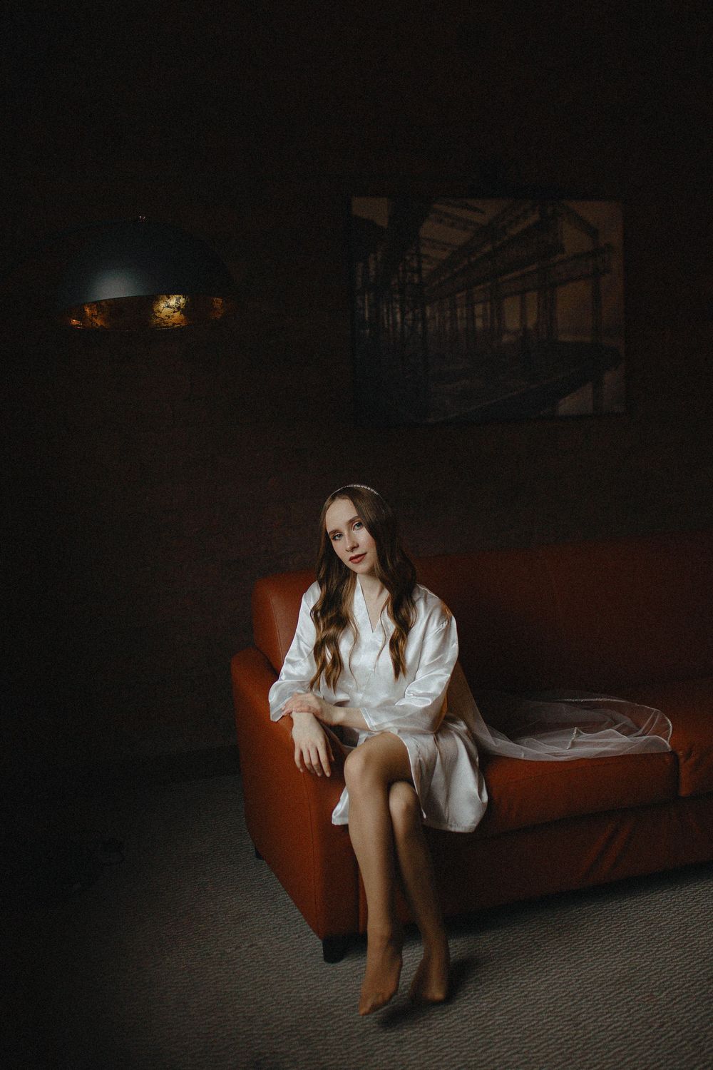 A figure in a white button-down shirt poses on a red vintage couch in a dark moody setting.