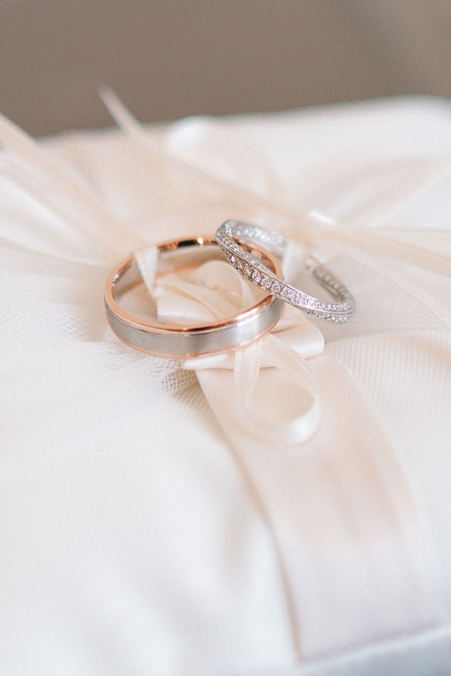 Two elegant wedding rings, one gold band and one diamond eternity band, resting on a white satin ring pillow with ribbon.