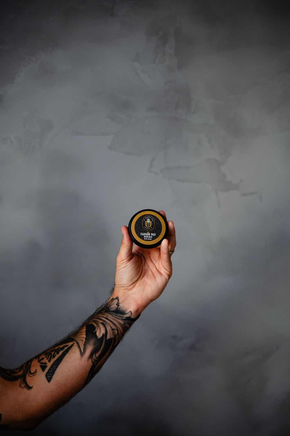 A tattooed arm holds a black hockey puck against a dark moody background.