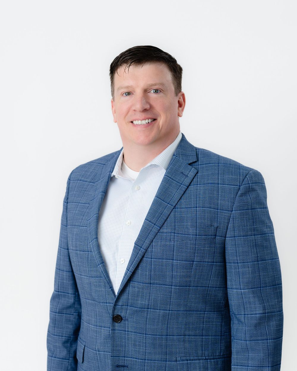 Professional wearing a blue plaid blazer and white shirt poses against white background for headshot portrait.