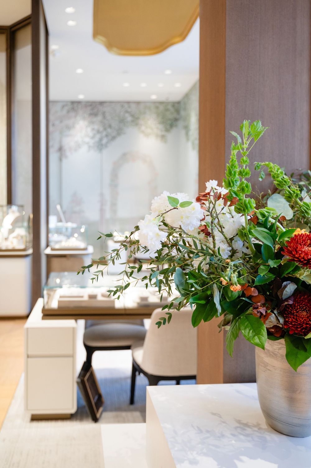 Elegant floral arrangements with greenery and red blooms decorate display cases in a high-end jewelry store interior.