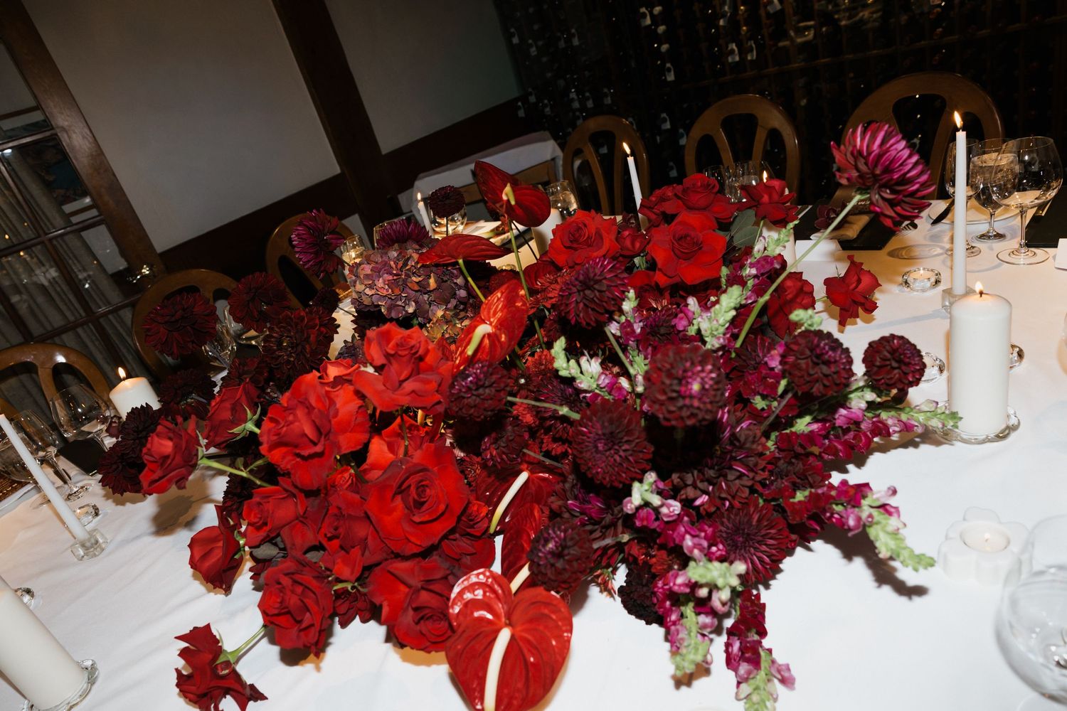 Elegant table settings at a formal event with white linens, red floral centerpieces, and crystal glassware.