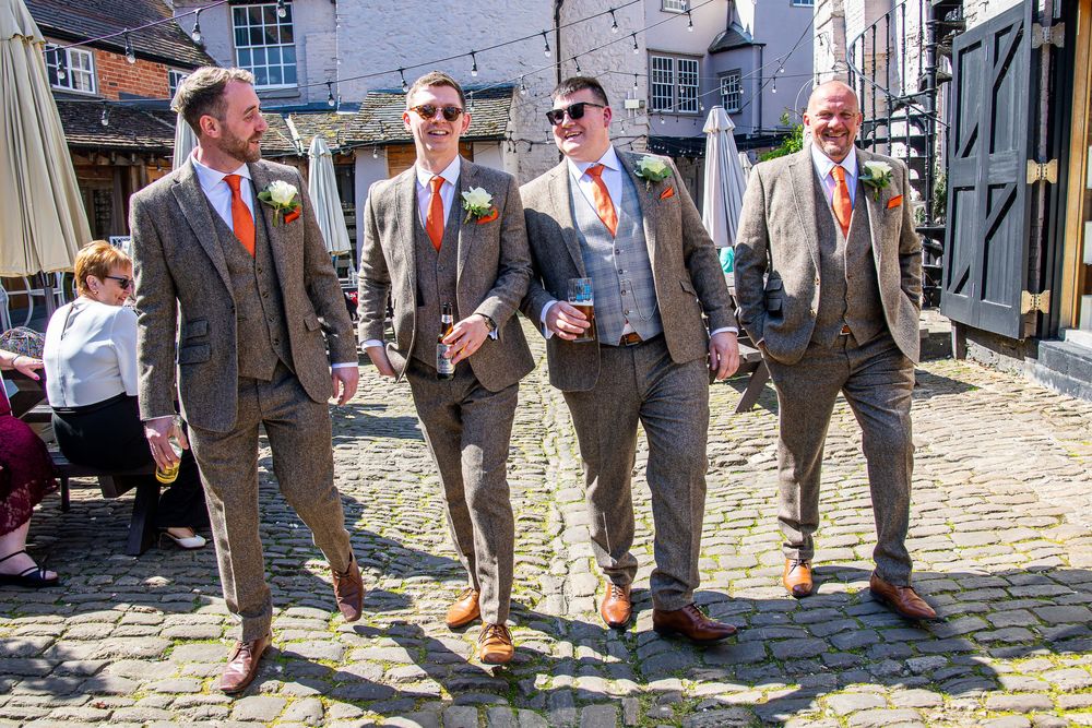 Groomsmen in gray suits posing on cobblestone street.