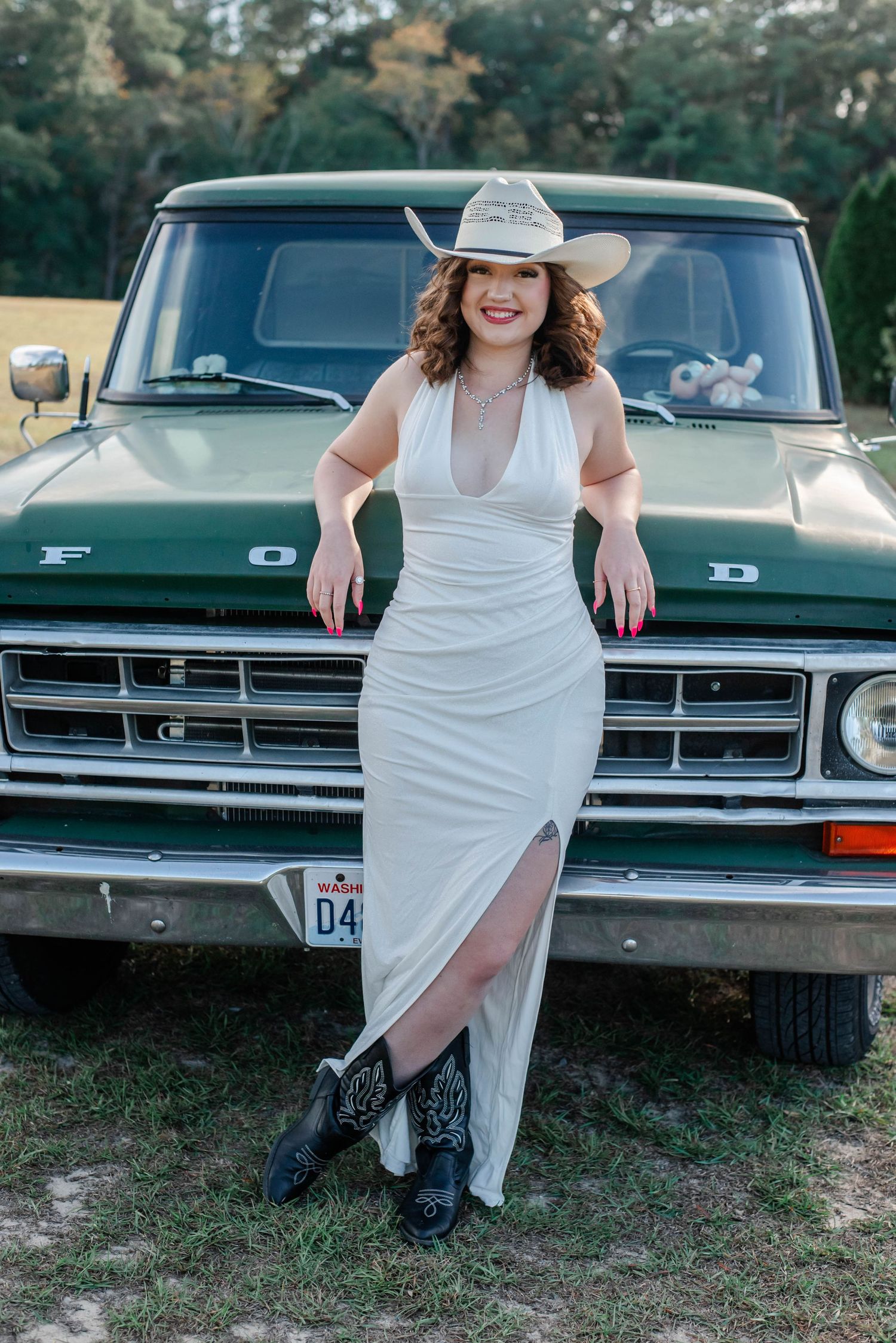 A white dress and cowboy boots styled photo shoot featuring poses in front of a vintage dark-colored car.