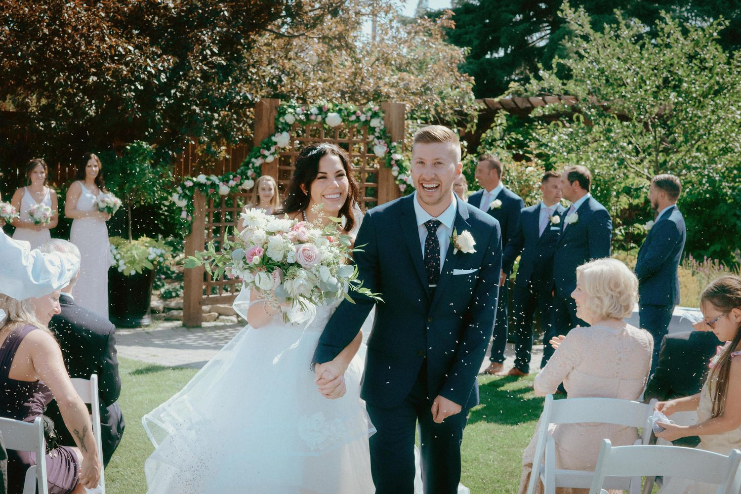 Bride and groom exit their outdoor Calgary Zoo wedding ceremony captured by a Calgary wedding photographer on a sunny summer day.