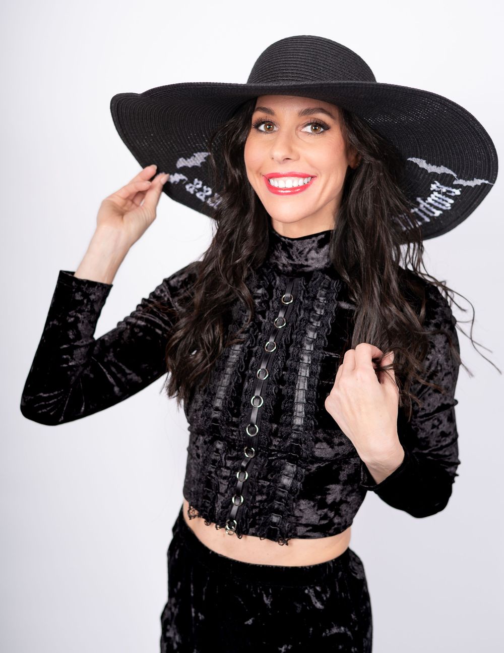 Model wearing a black lace crop top and wide-brimmed hat in studio lighting.