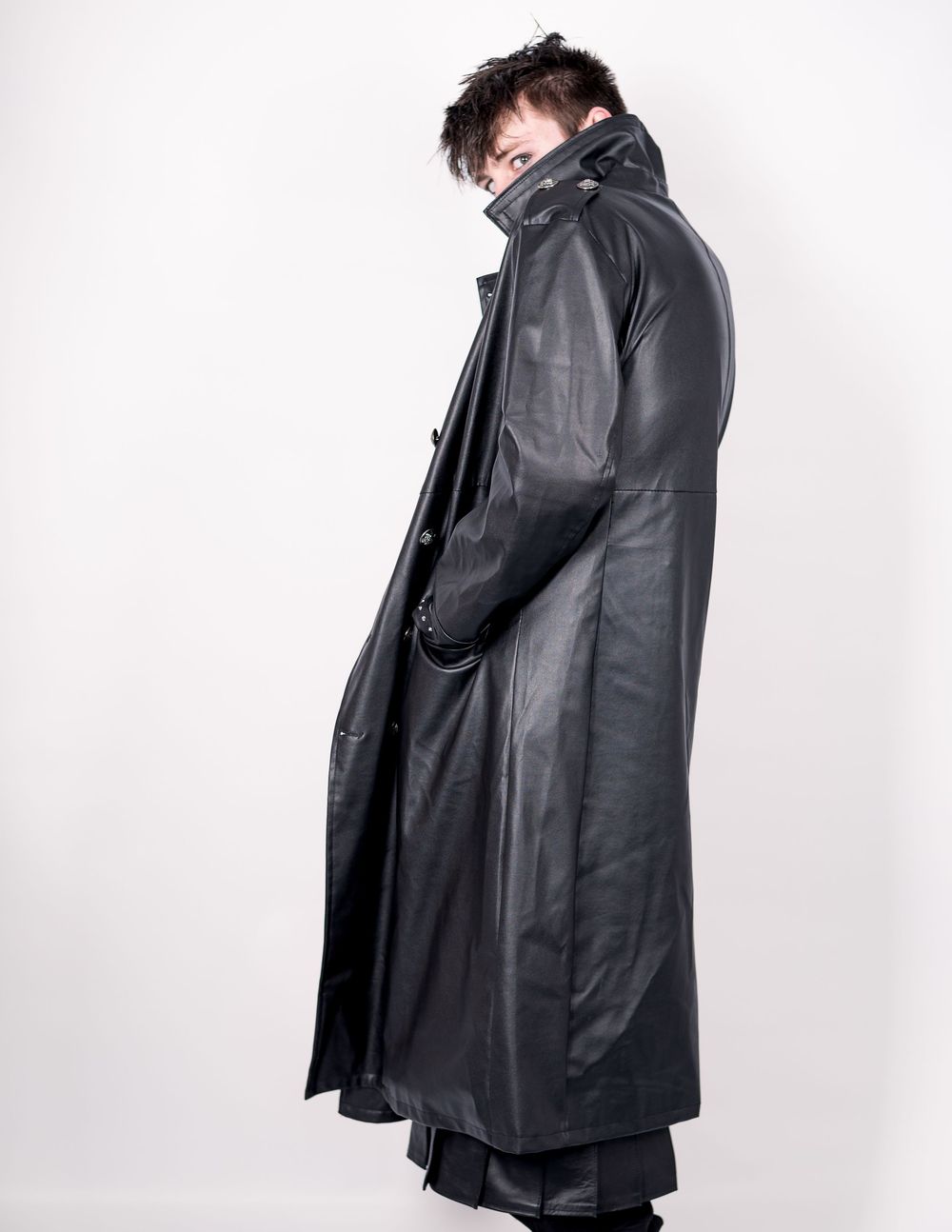 Long black leather trench coat styled in dramatic gothic fashion against white background.