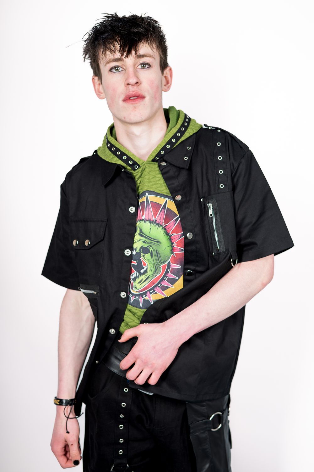 Fashion model wearing black button-up jacket over green hoodie with punk-inspired styling.