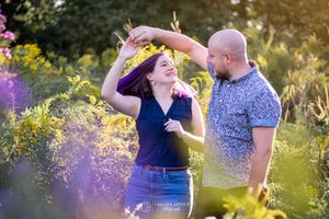 Two people share a playful moment dancing together outdoors among purple wildflowers at sunset.