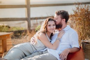 A romantic couple sits together on outdoor furniture during golden hour among autumn foliage.