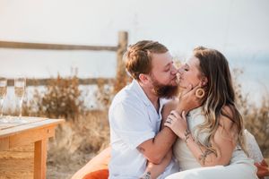 A romantic couple shares a tender kiss while sitting outdoors during golden hour on a rustic bench.