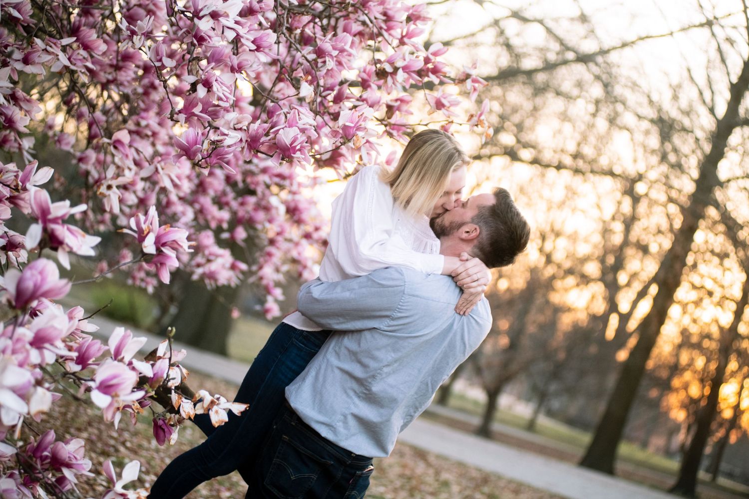 Romantic spring scene with couple embracing by blooming pink magnolia tree at sunset.