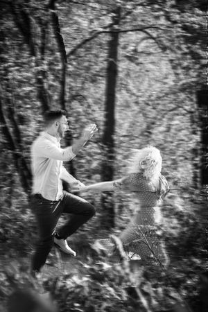 A playful black and white portrait of two people jumping in a forest, creating a whimsical moment in nature.