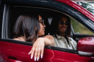 Two people in a red car sharing a moment while sitting in the front seats and enjoying music together.