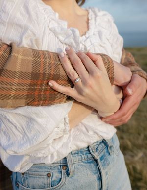 Close-up of hands showing an engagement ring against white lace and plaid clothing details.