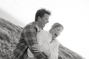 Black and white portrait of couple laughing together on windswept coastal hillside.