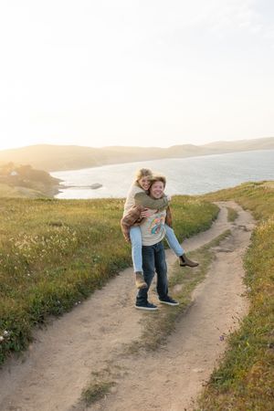 Couple playfully spinning and dancing together on a scenic coastal trail at sunset overlooking the ocean.