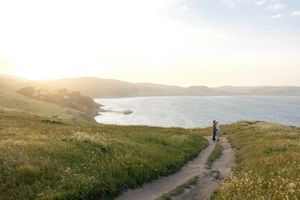 Scenic coastal hiking trail winding along green cliffs overlooking the ocean at sunset.