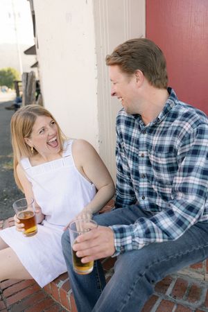 Couple sharing laughs and drinks while sitting on brick steps outdoors.