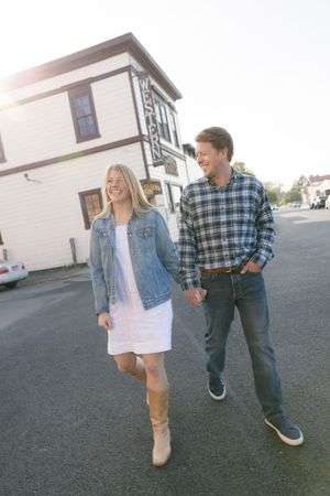 Couple walking hand in hand past white building on sunny day, woman in denim jacket and dress.