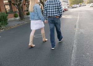 Two people walking together on a paved street, one wearing a denim jacket and the other in a plaid shirt and jeans.