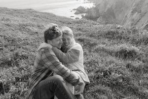 Vintage black and white photograph of couple cuddling on coastal clifftop overlooking ocean.
