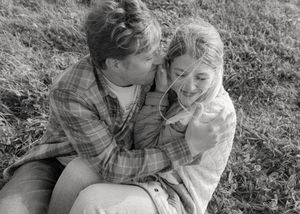 Black and white photo of couple laughing together while embracing on grassy hillside.