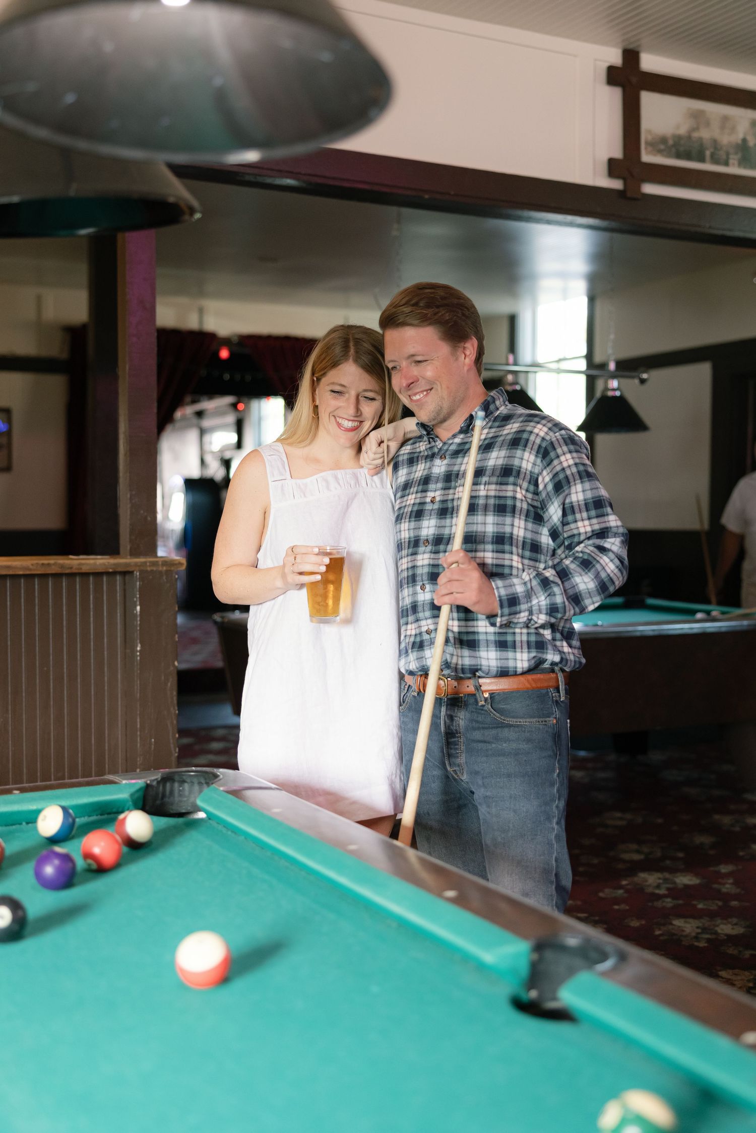 Couple playing pool together in a bar setting with one person showing proper shooting technique.