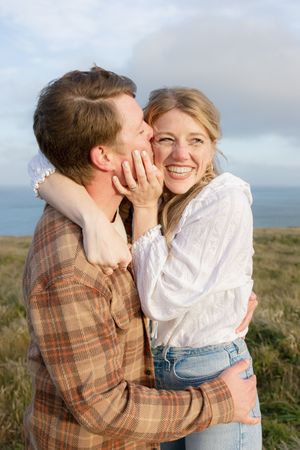 Joyful couple sharing an intimate moment while embracing on a coastal hilltop at sunset.