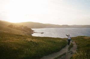 Person walking along scenic coastal trail during golden sunset with expansive ocean views.