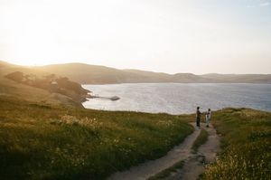 Wide landscape shot of a coastal trail with distant figures silhouetted against the ocean view.