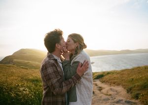 Romantic couple sharing tender moment on coastal path with sunset and ocean backdrop.