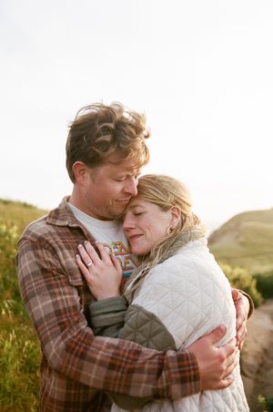 Intimate embrace between couple on hillside during golden hour.
