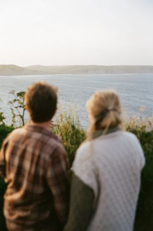 Two people sit together looking out over a scenic coastal view at dusk.