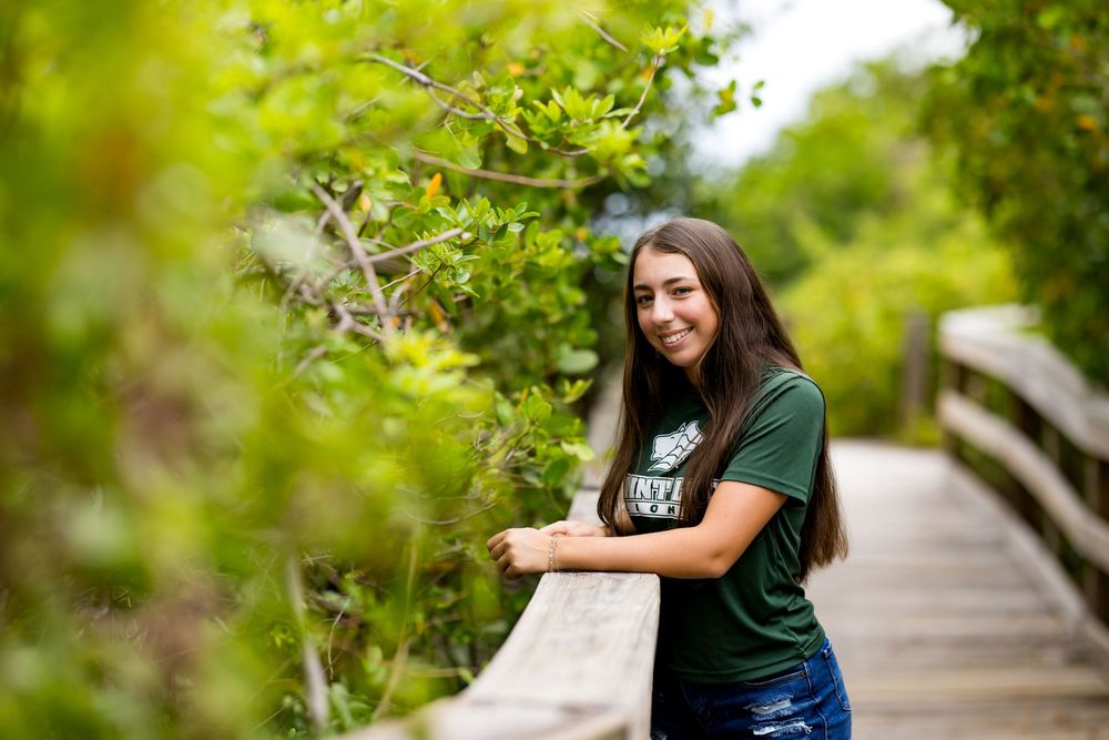 Standing by wooden railing on nature boardwalk wearing green university shirt.